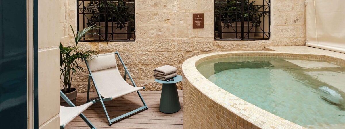 Poolside patio with two light-blue framed chaise lounges, a small table with folded towels, beside a curved tiled pool.