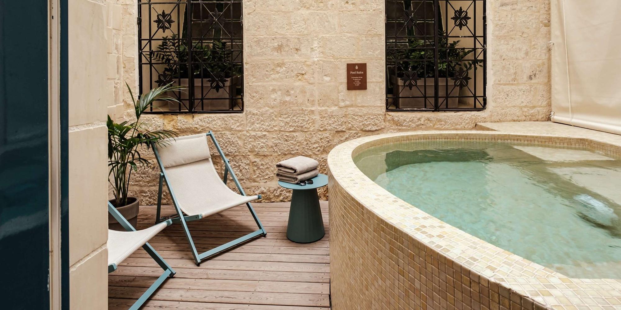 Poolside patio with two light-blue framed chaise lounges, a small table with folded towels, beside a curved tiled pool.