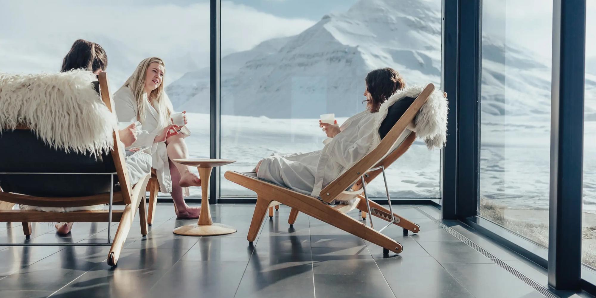 An image of a relaxation room overlooking the mountains featuring women wearing gowns at Deplar Iceland. Alpine relaxation room overlooking the mountains featuring people at Deplar Iceland.