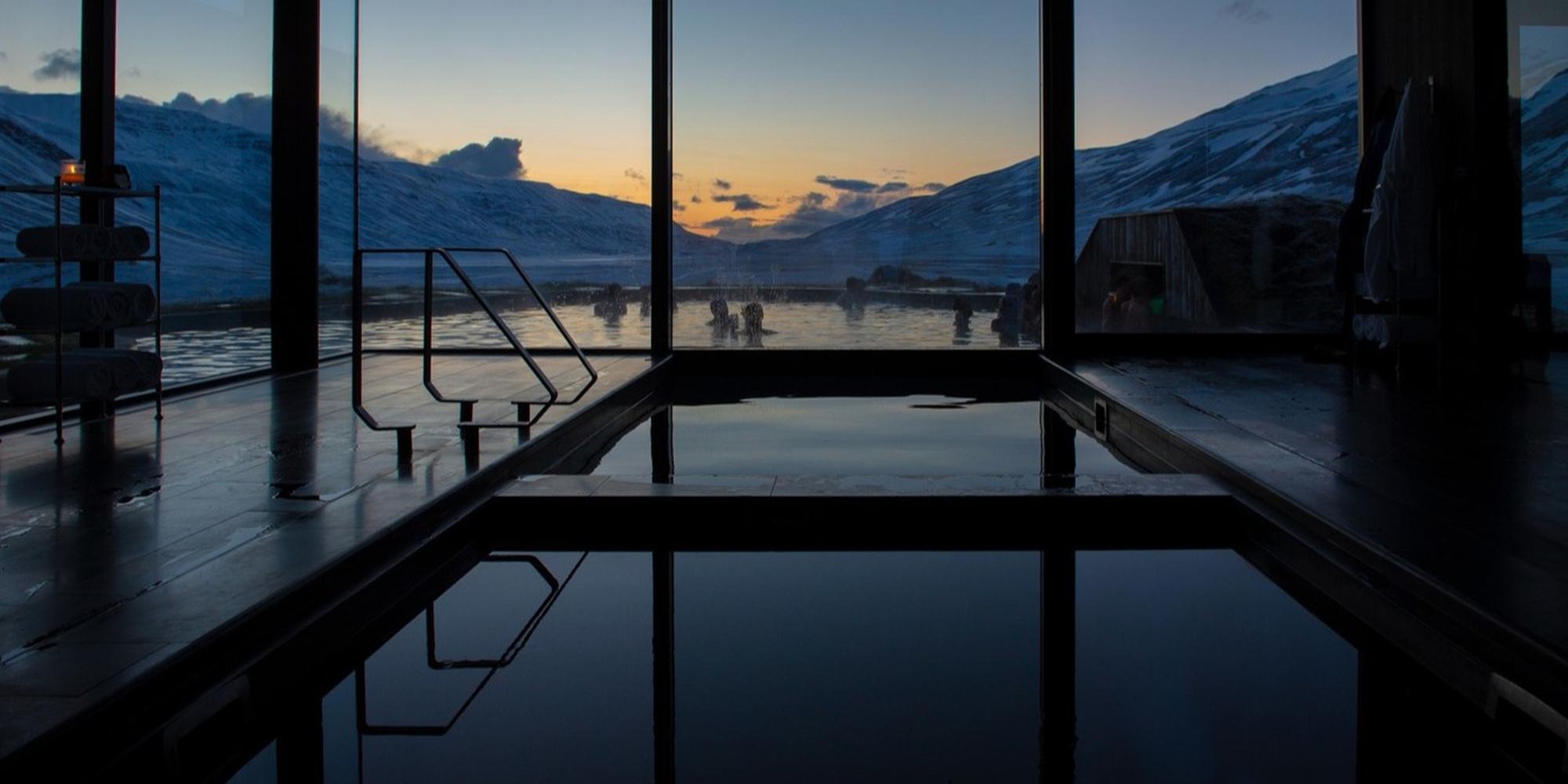 A picture of indoor pool at the Deplar Iceland that shows a panoramic view of a coastal sunset or sunrise. An indoor pool at the Deplar Iceland.