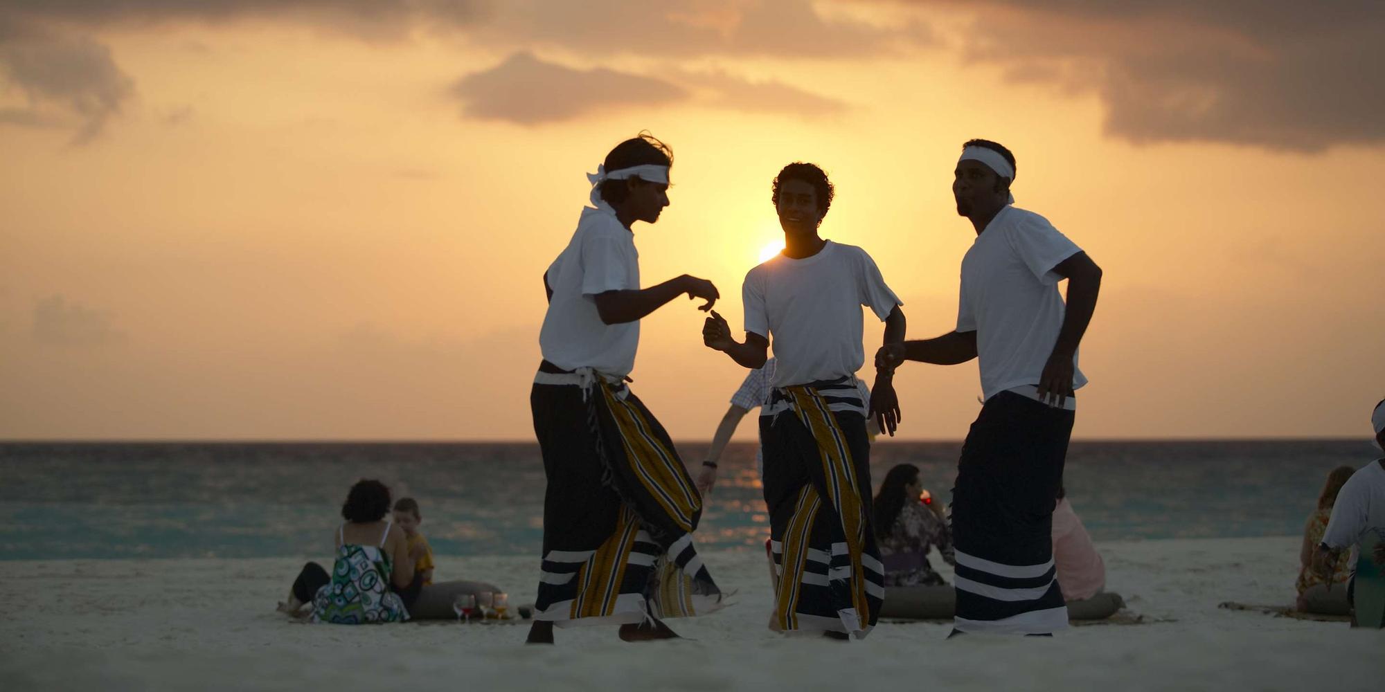 The imahe depicts performers wearing traditional attire celebrating at sunset on Soneva Fushi in Maldives. Performers wearing traditional attire celebrating at sunset on Soneva Fushi in Maldives.