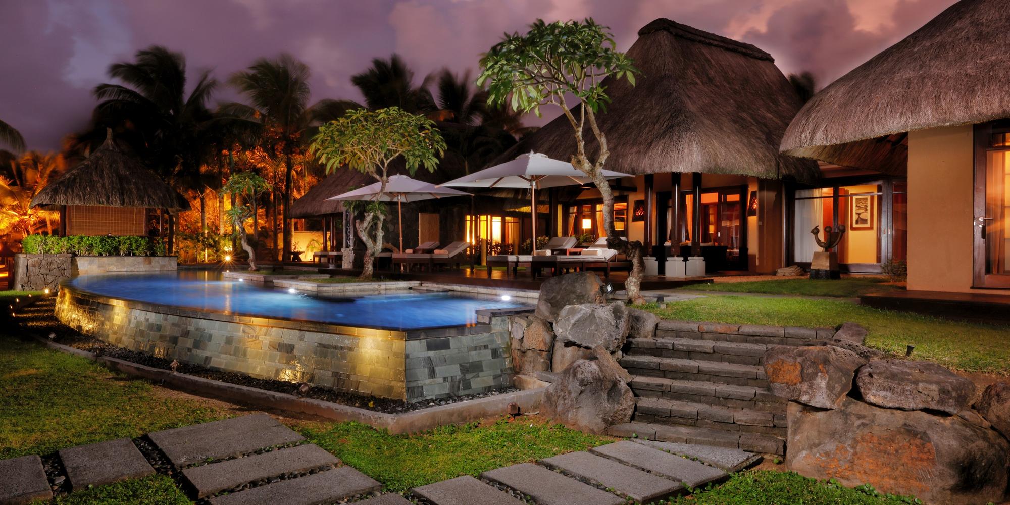 An image of a luxury resort-style villa in Shanti Maurice in Mauritius featuring a beautifully lit private swimming pool surrounded by lush greenery. Luxury resort-style villa in Shanti Maurice in Mauritius.