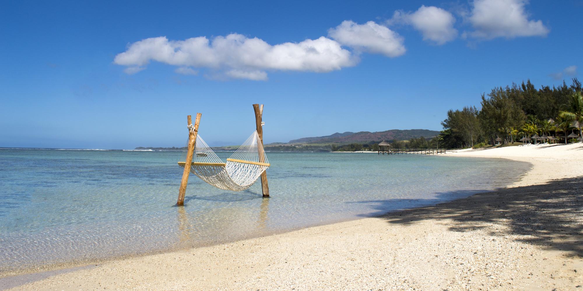 A picture of hammock which is directly positioned over the shallow water in Mauritius. A hammock over a turquoise lagoon in Mauritius.