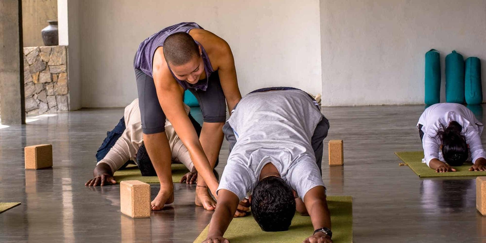 A yoga where a yoga instructor providing hands-on alignment adjustment to a guest. 