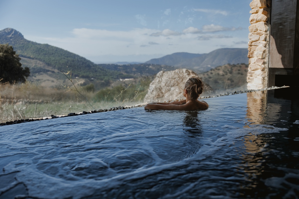 A person relaxes in an infinity pool overlooking a serene mountainous landscape. The scene conveys tranquility and a strong connection to nature, the inverse of being held captive in the digital world. YOLO Travel, in partnership with La Donaira, provides the ultimate setting for a successful digital retreat. A person relaxes in an infinity pool overlooking a serene mountainous landscape. The scene conveys tranquility and a strong connection to nature. Escape to La Donaira with YOLO Travel for a digital detox retreat.