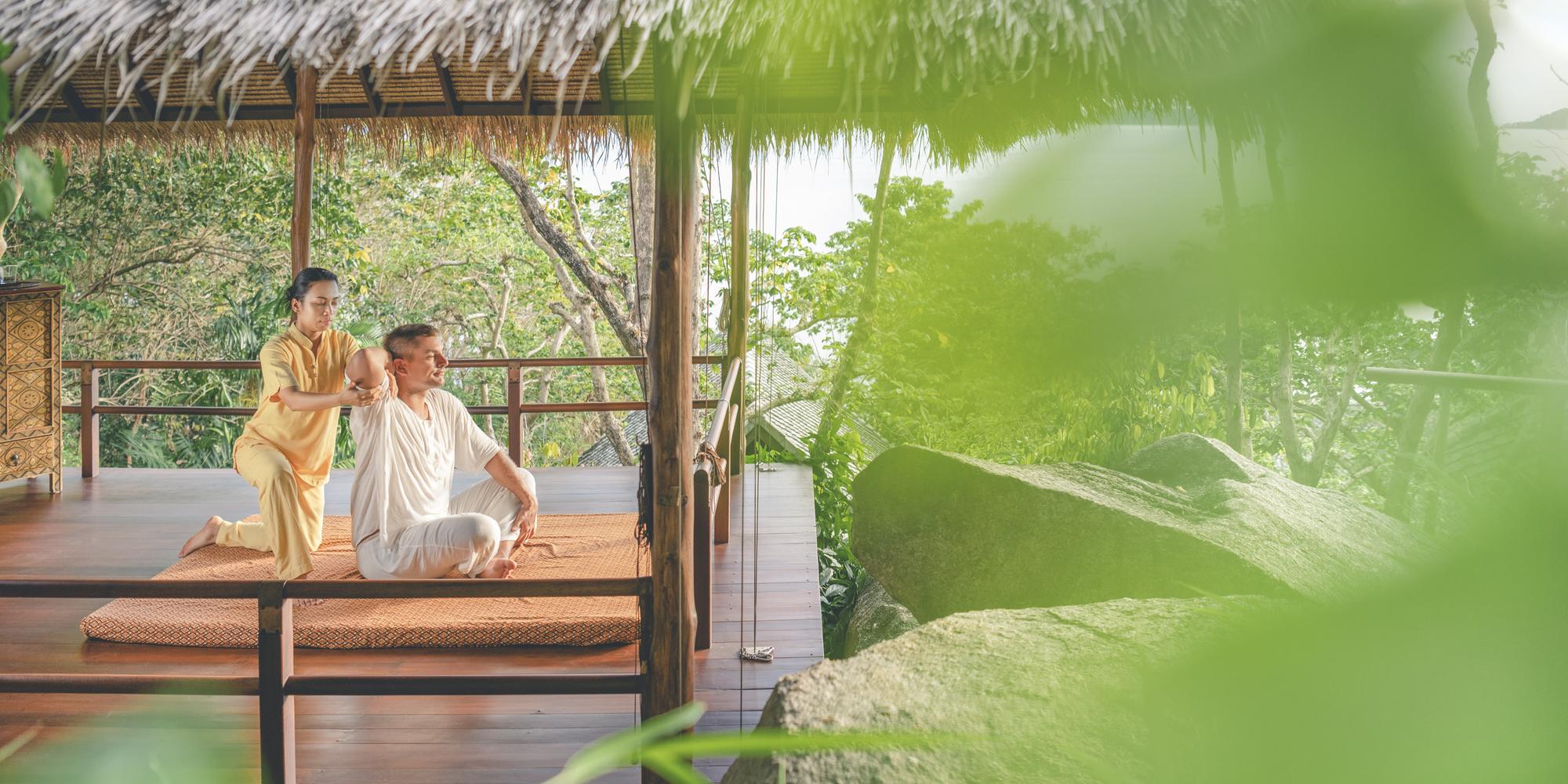 A traditional Thai massage taking place in an open-air sala at a wellness resort like the Kamalaya in Asia.