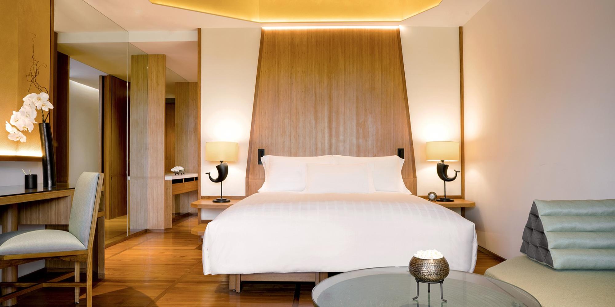 A luxury hotel room featuring prominent dark wood paneling behind a white-accented bed at Chiva-Som.