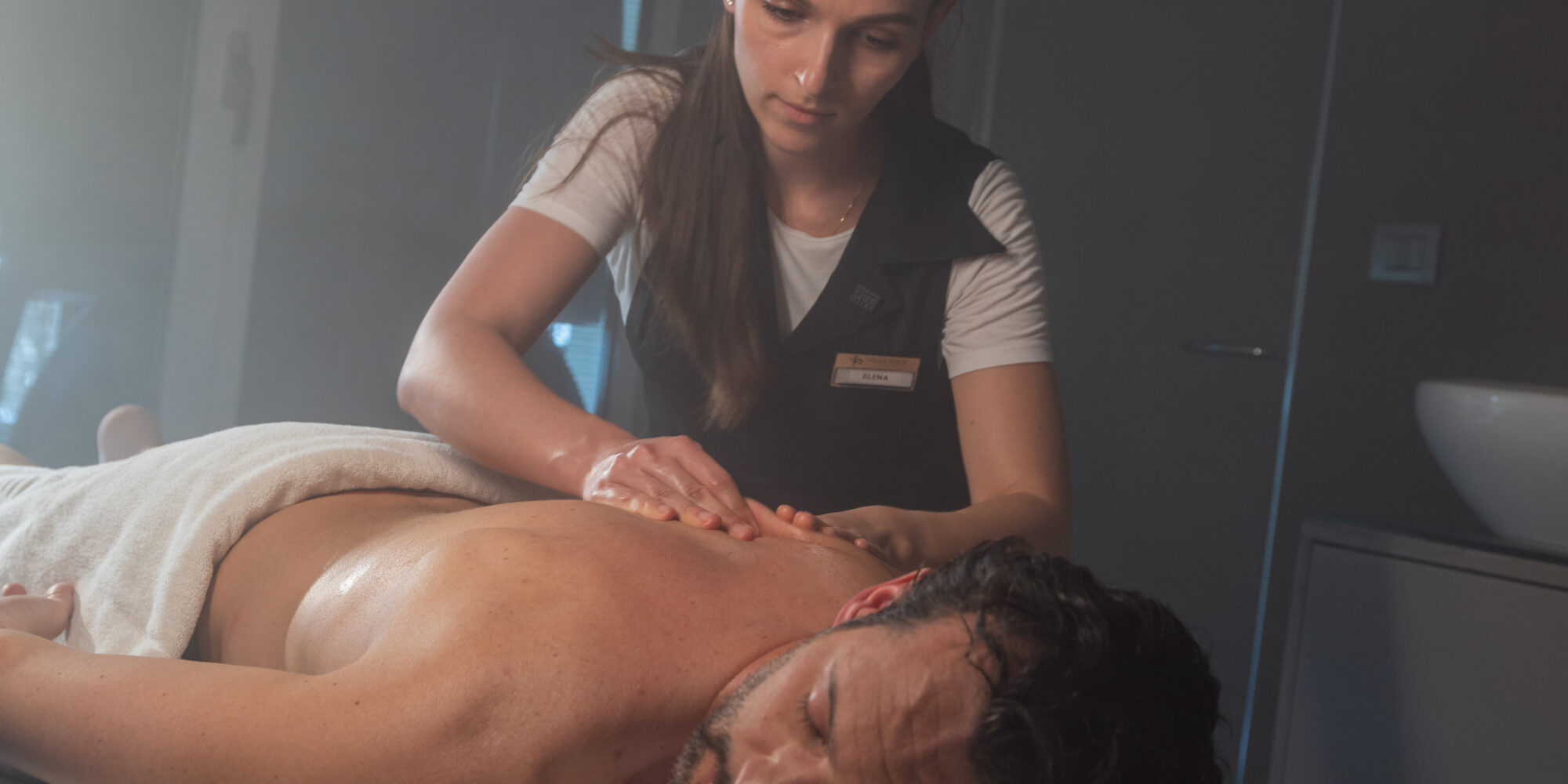 A spa employee in a black vest preforming a treatment on a client.