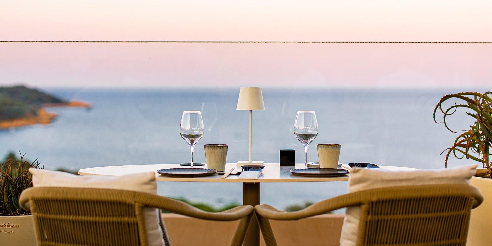 A dining table featuring a woven rattan chairs paired with minimalist place setting at La Réserve Ramatuelle Hotel, Spa & Villas, Europe. A dining table featuring a woven rattan chairs paired with minimalist place setting at La Réserve Ramatuelle Hotel, Spa & Villas, Europe.