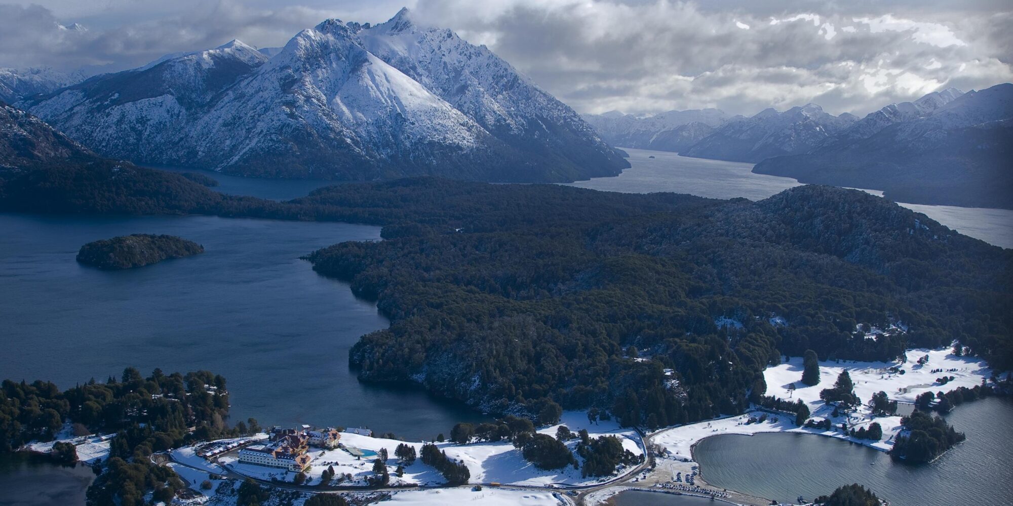 The aerial scene showing a cold, mountainous region, featuring a snow-covered peak, deep blue water and dense forests. The aerial scene showing a cold, mountainous region, featuring a snow-covered peak, deep blue water and dense forests.