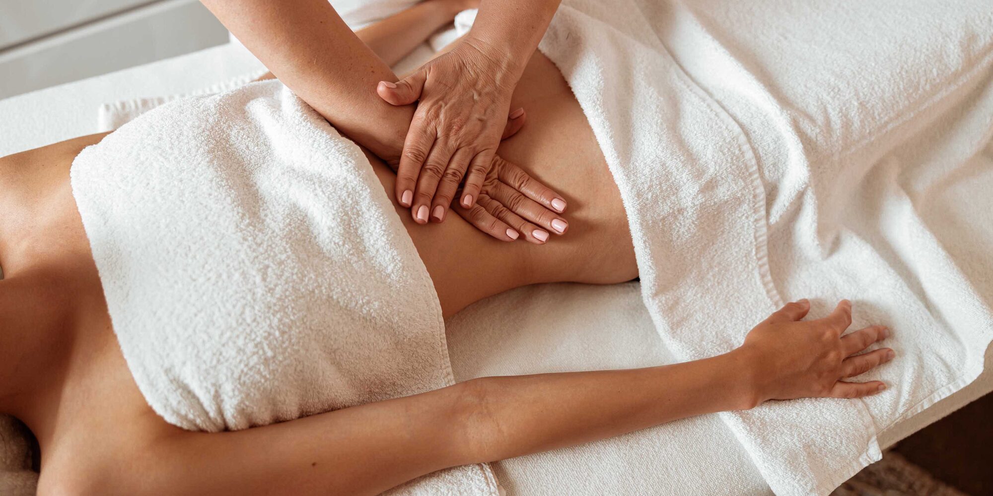 A guest in white towels receiving an abdominal massage. A guest in white towels receiving an abdominal massage.